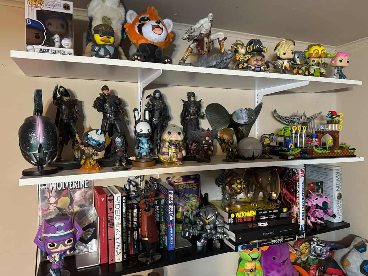 A picture of three distinct shelves holding various gamer regalia and books.
